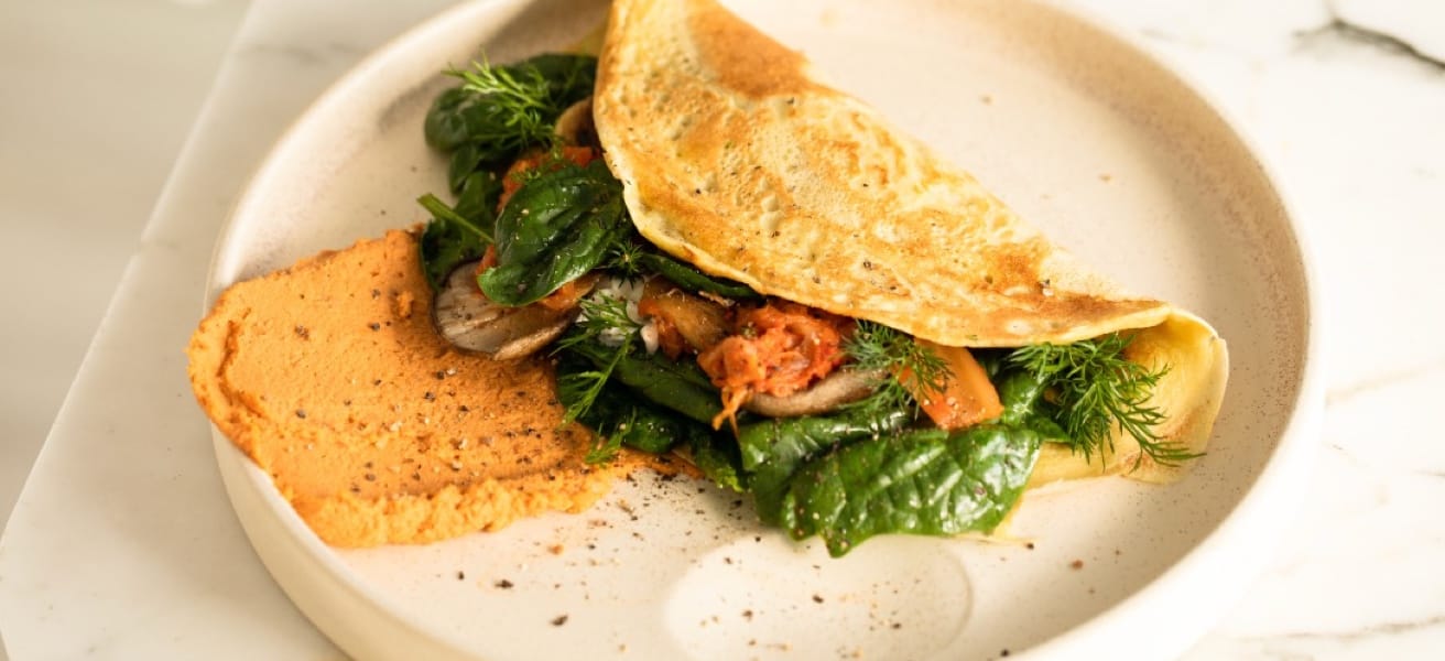 folded omelette stuffed with spinach, tomato and mushrooms on an off-white plate